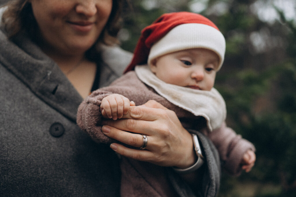 Mama mit Baby Tochter auf dem Arm hält die Finger der Mama bei Familien Outdoorshooting