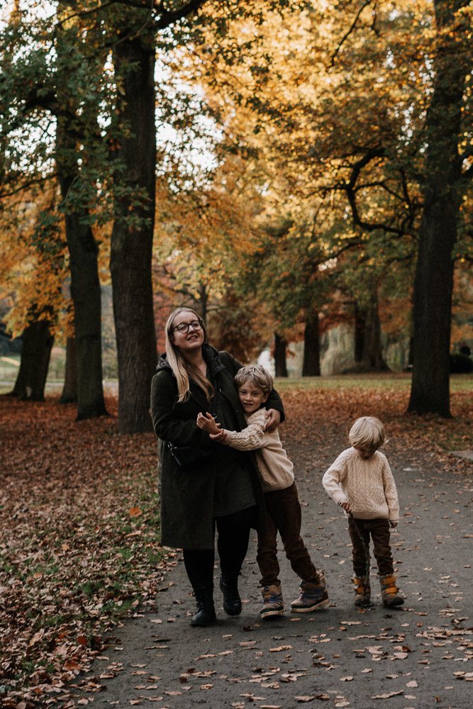 Mama und Söhne laufen albernd durch Park bei Familien Outdoorshooting