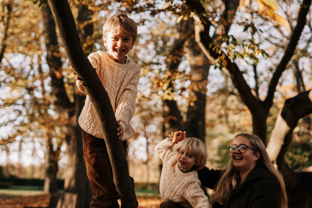 Mutter und Söhne kletternd auf Baum bei einem Herbstspaziergang fotografiert im Park