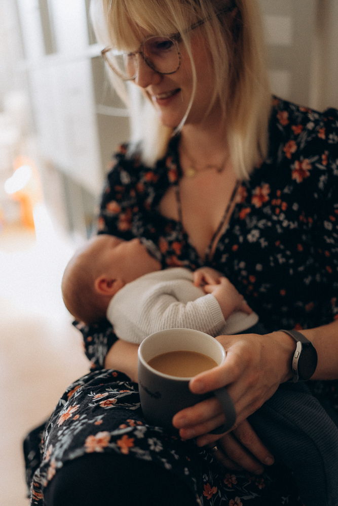 Mutter mit Baby auf dem Arm trinkt Kaffee