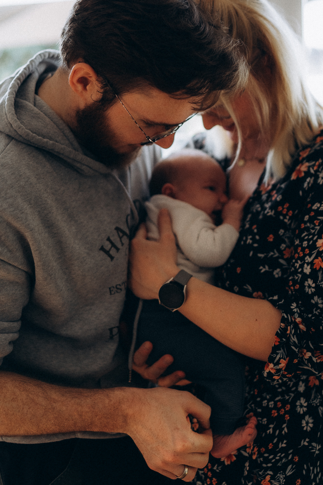 Baby mit Mama und Papa innig kuschelnd bei Neugeborenen Fotoshooting