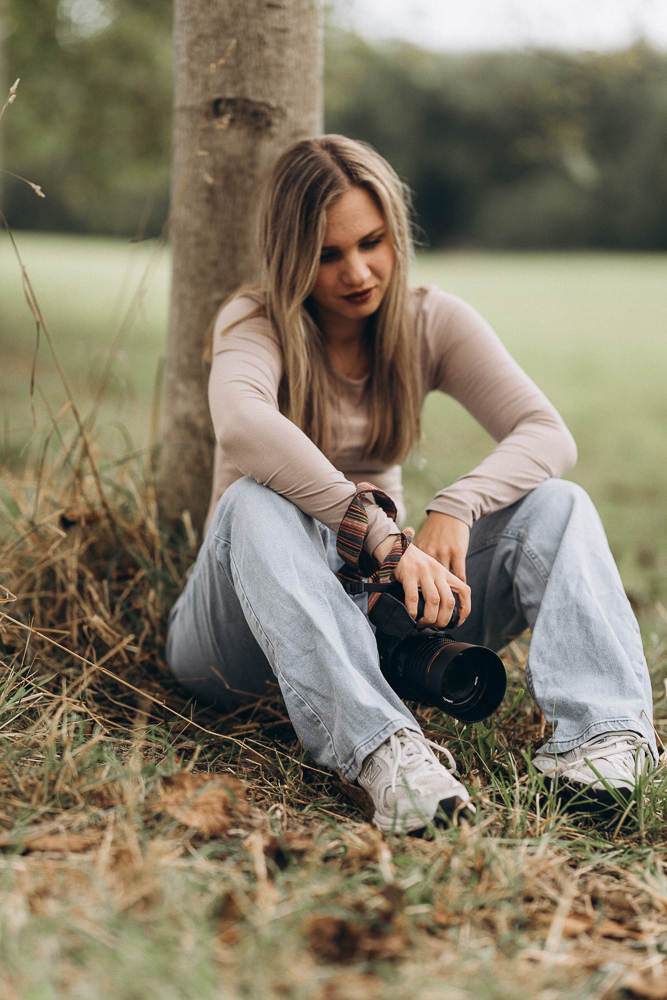 Portraitshooting Frau mit Kamera sitzend vor einem Baum