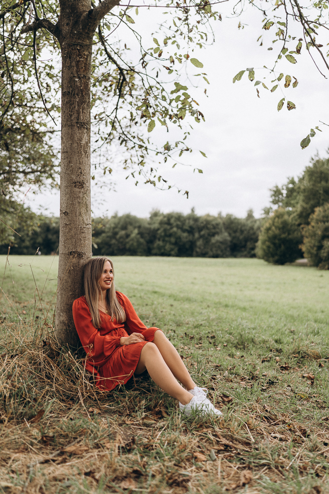 Portraitshooting Frau in rotem Kleid sitzt vor Baum